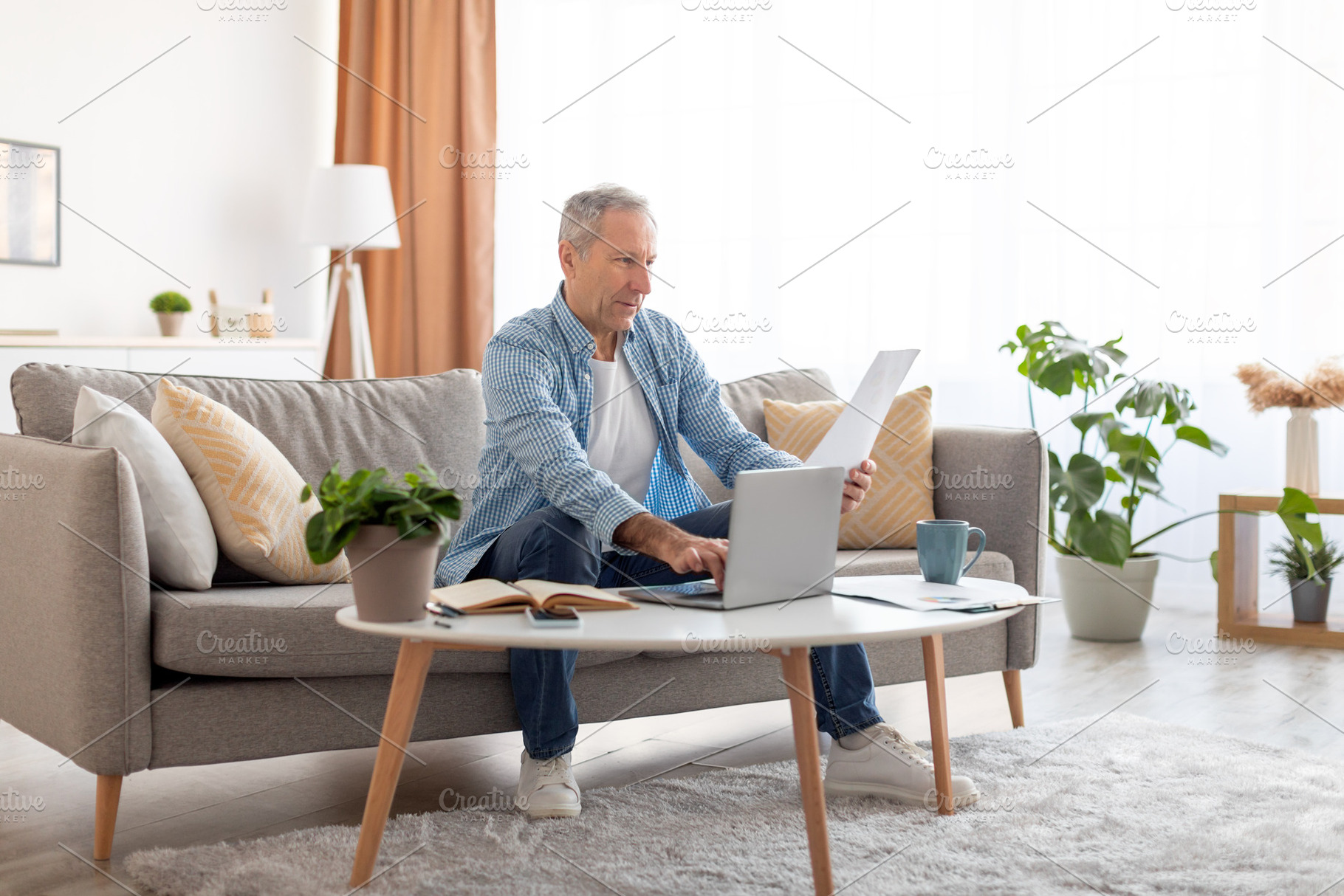 Man holding documents reading report working on laptop at home, a Photo by Prostock-Studio