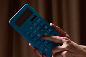 A person calculating on a blue calculator against a dark backgro, a Business Photo by ndanko
