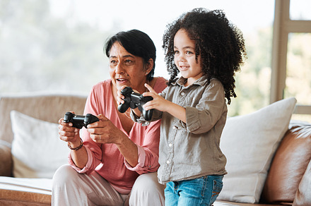 Grandmother, kid and gaming on sofa, controller and happy together with bond, care and love in family home. Senior woman, young child and playing with video game, esports and excited in living room, a Photo by Peopleimages.com