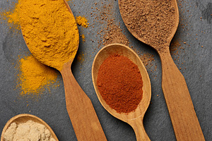 Multicolored ground spices in wooden spoons on a black board,, a Food & Drink Photo by ndanko