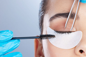 Woman, lashes and tweezer with mascara, studio closeup and makeup artist in gloves, hands and extension. Girl, model and zoom of face for beauty, cosmetics and brush for aesthetic by gray background, a Photo by Peopleimages.com