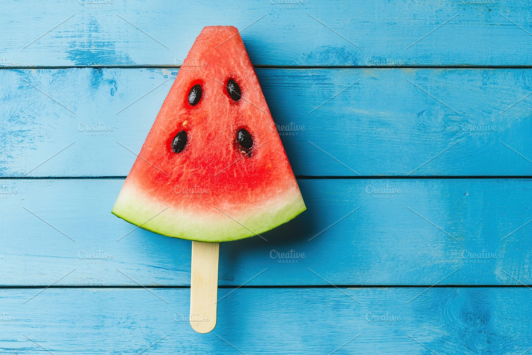 Refreshing watermelon slice shaped like an ice pop on blue wooden surface, a Food & Drink Photo by AlyaAnd