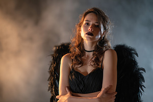 Mysterious woman with black wings poses in dramatic lighting during a creative, a Photo by AlyaAnd