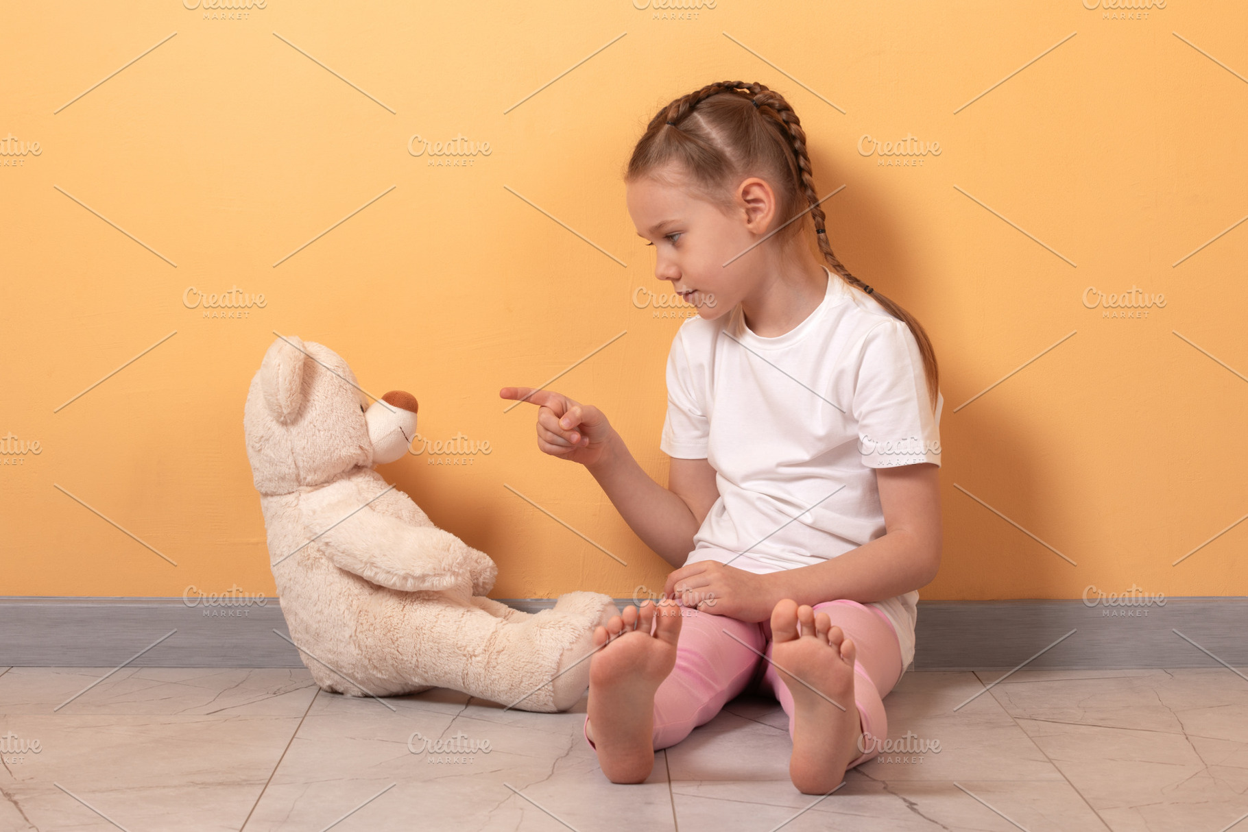 Young girl sitting on floor pointing at plush teddy bear, playfu, a Person Photo by Ales Munt