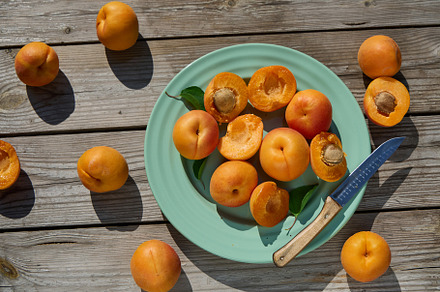 Whole and halved apricots on turquoise plate with knife on rustic wooden table