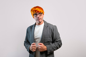 Man wearing orange wig and glasses looking at camera, a Person Photo by karrastock