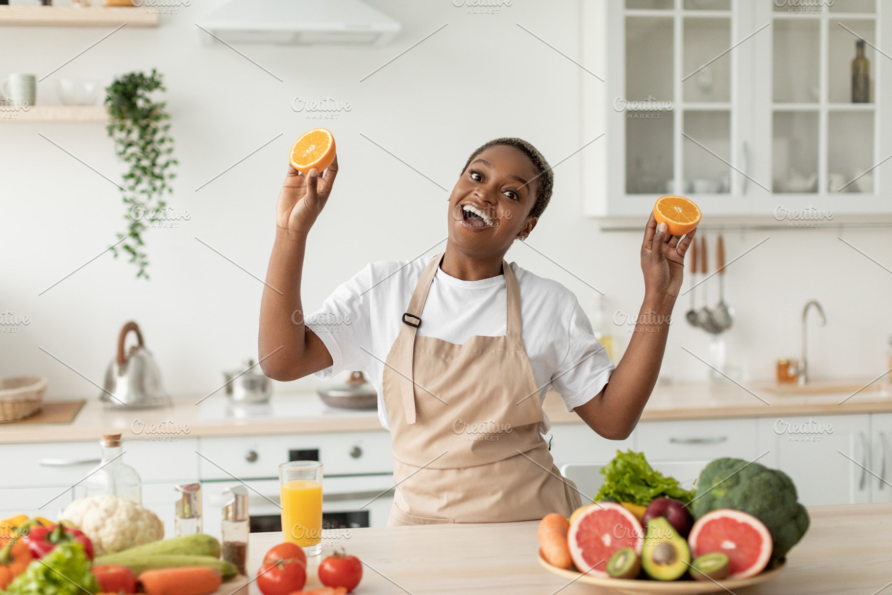 Glad emotional young black woman in apron have fun on minimalist kitchen interi, a Person Photo by Prostock-Studio