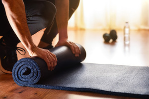 Person in sportswear and sneakers preparing a mat for exercise, a Sports & Recreation Photo by Davizro's Market