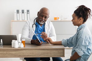 Experienced black doctor explaining treatment plan to female patient, a Photo by Prostock-Studio