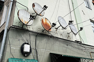 Rusty satellite dishes on a building facade with attached electrical wires, a Photo by AS photostudio
