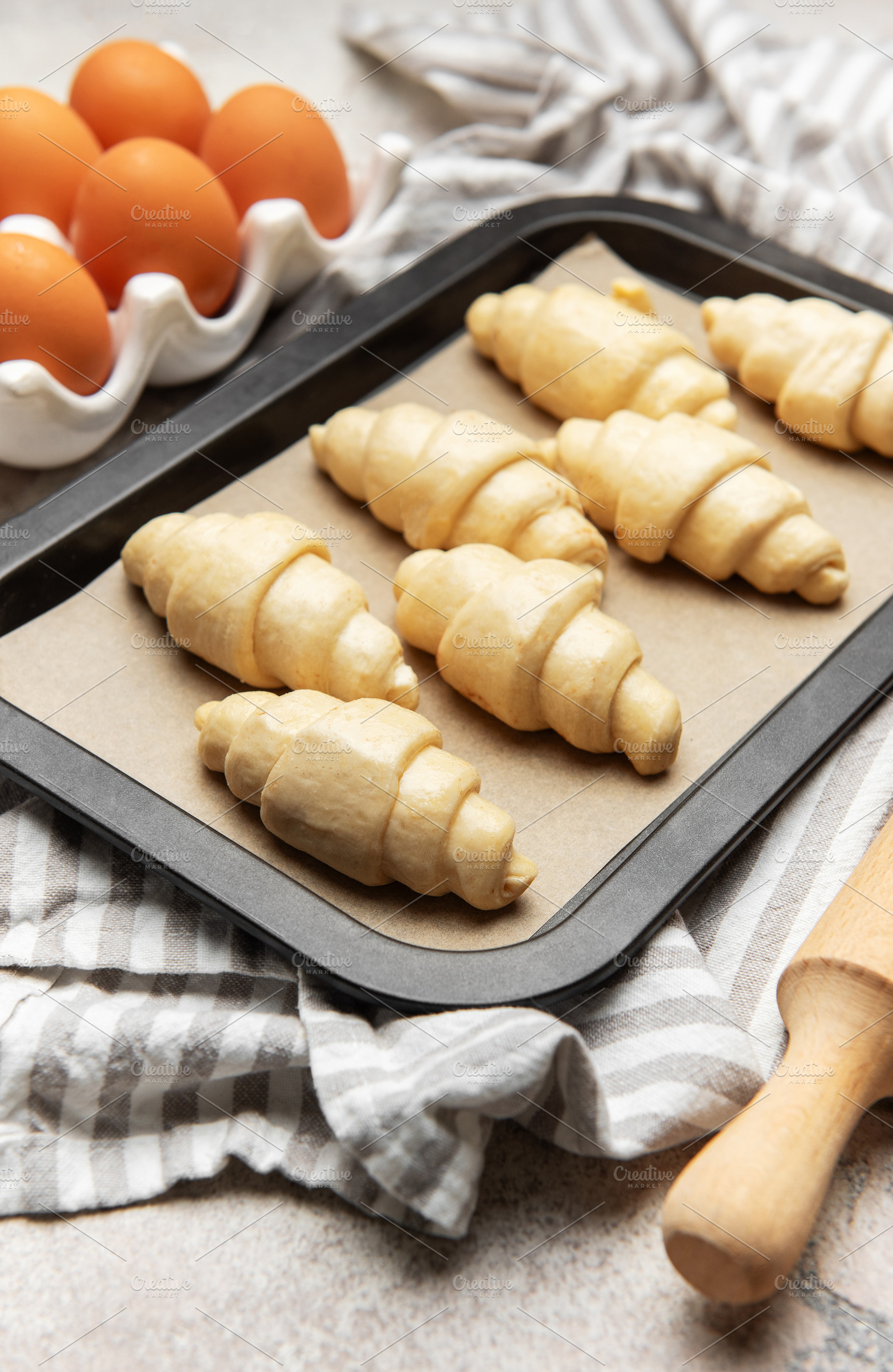 Freshly made croissants resting on baking sheet await oven's war, a Food & Drink Photo by Olena Rudo