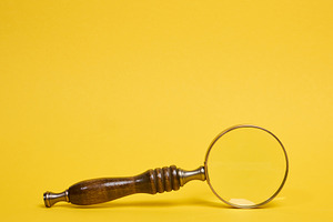 A vintage magnifying glass with a wooden handle lying on a yello, a Business Photo by ndanko