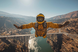 Skydiver in Vibrant Gear Soaring Over Scenic Mountain Bridge, a Sports & Recreation Photo by Ocean Digital Art