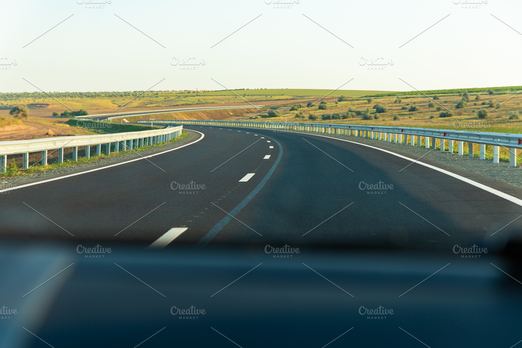 Smooth asphalt highway curving through open countryside with guardrails, clear, a Transportation Photo by Ales Munt
