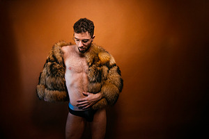 Confident man posing in faux fur jacket against orange background, a Photo by karrastock