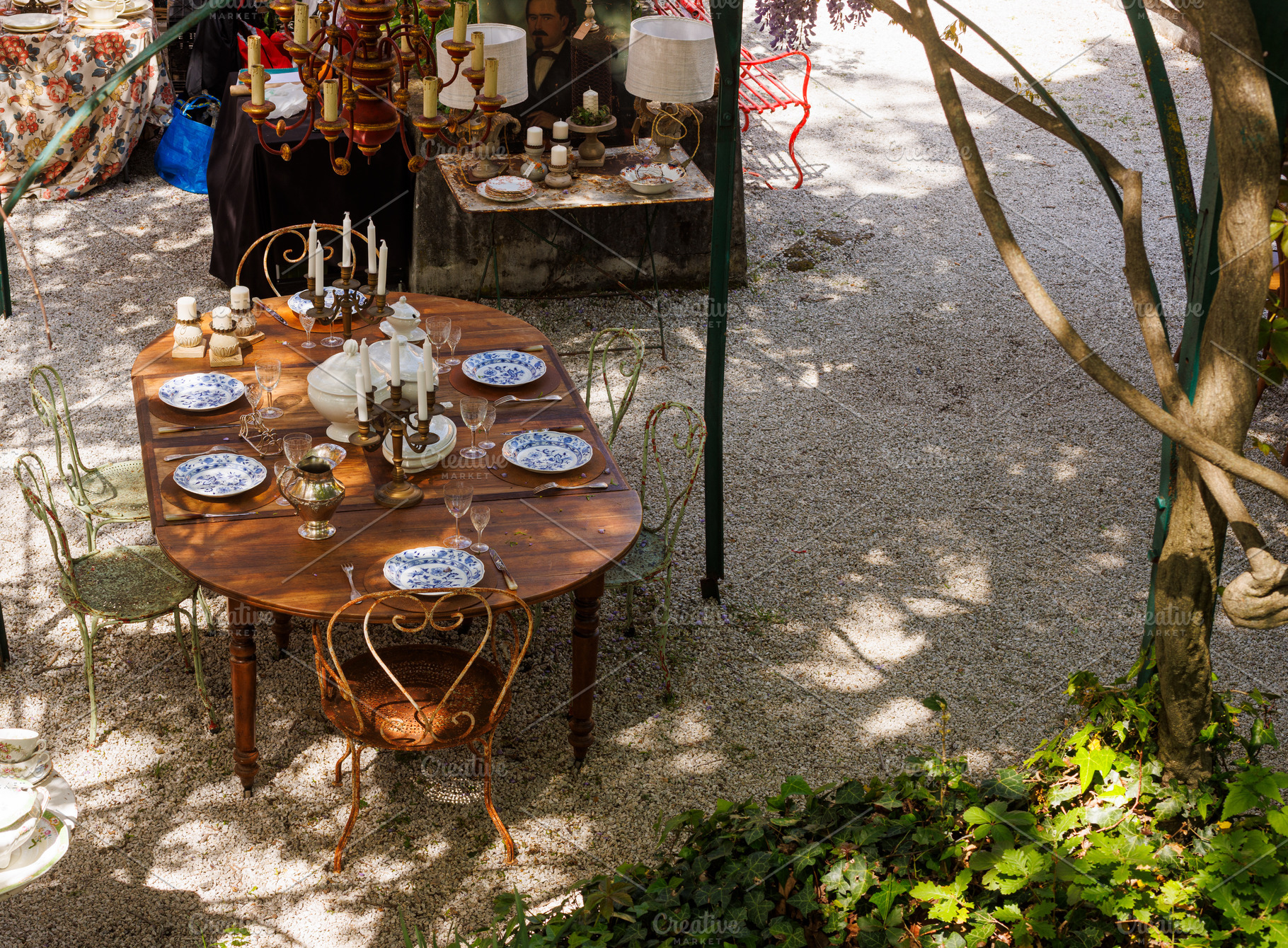 Wooden outdoor table in a garden courtyard set with vintage plates, a Food & Drink Photo by Bepslabor