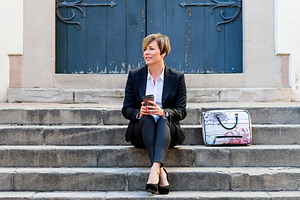 Businesswoman sitting on steps with coffee cup, a Photo by RF Images