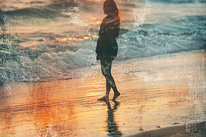 Silhouette of a woman walking along the shoreline during sunset, a Photo by AlyaAnd
