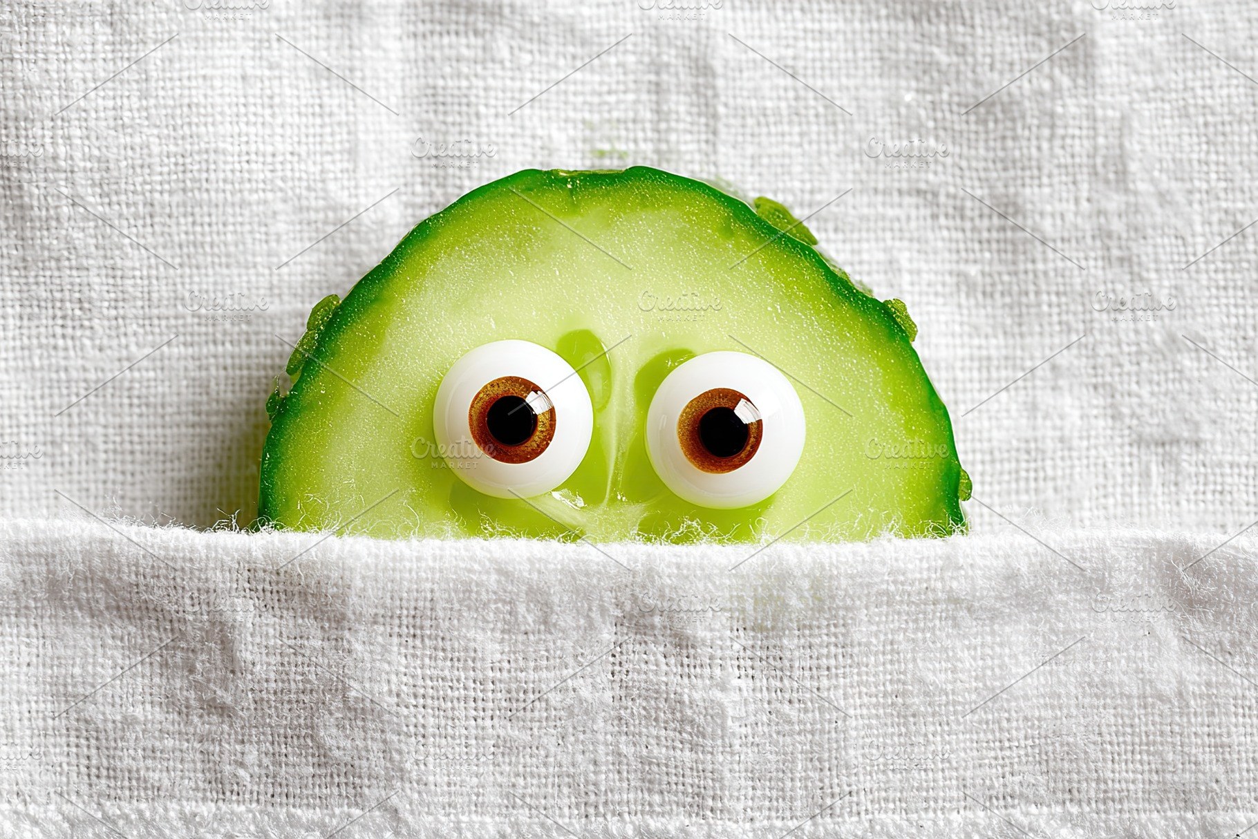 Cute cucumber slice peeking out from behind a white towel on a kitchen countert, a Food & Drink Photo by AlyaAnd