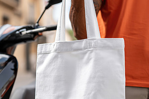 Delivery person holds white bag near scooter on city street during daytime, a Photo by AlyaAnd