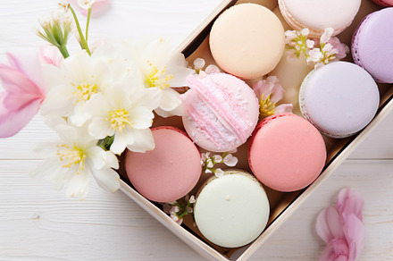 Colorful macarons dessert in box with flowers on wooden background, a Food & Drink Photo by AlyaAnd