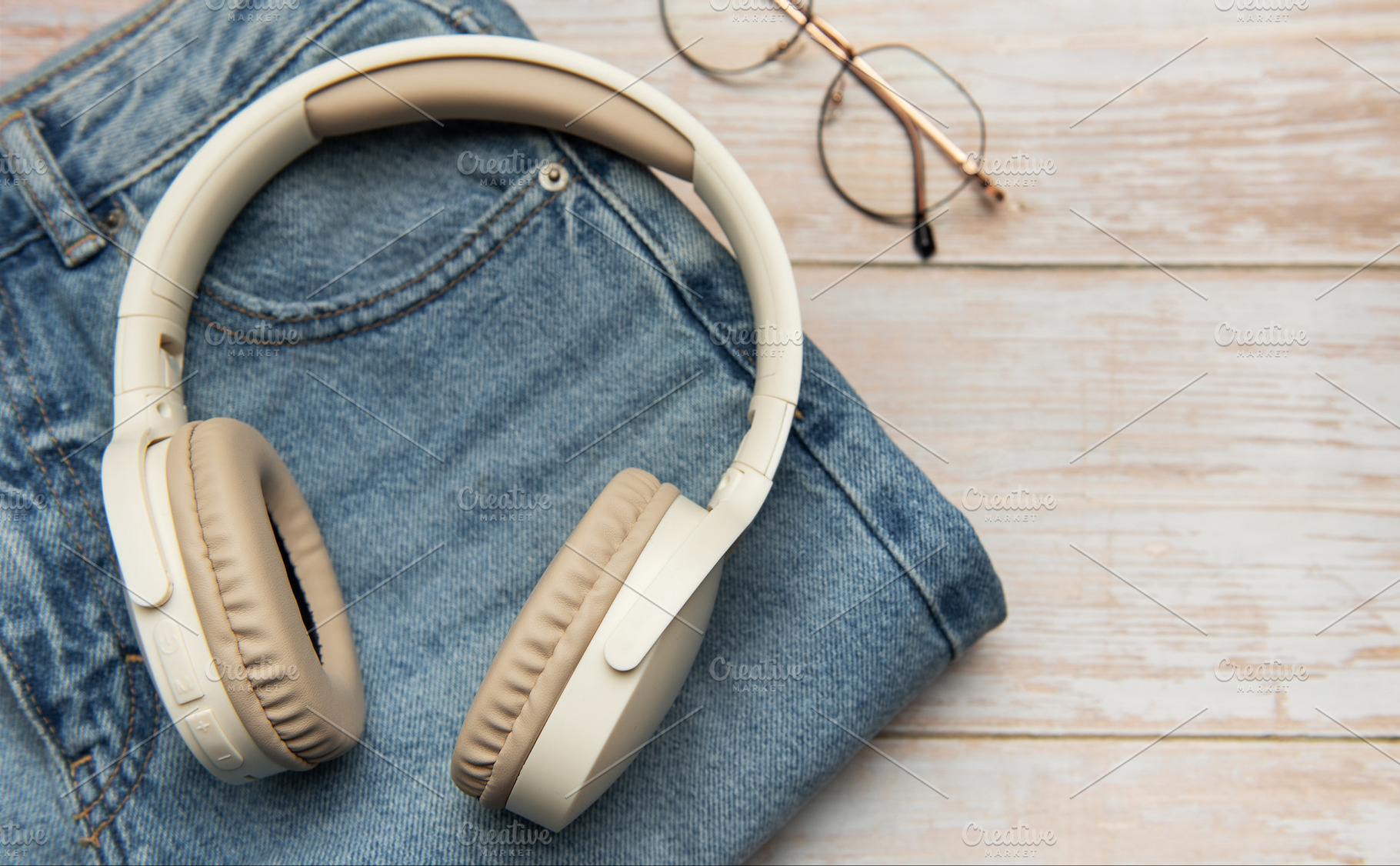 Wireless headphones lying on folded jeans and eyeglasses on wood, a Business Photo by Olena Rudo