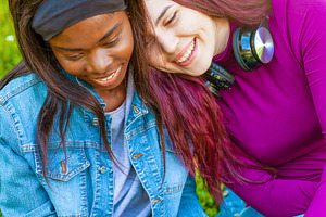 Two happy students using laptop and smiling in a park, a Person Photo by Antonio Gravante Market
