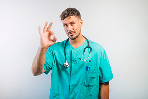 Male doctor in medical uniform making an “OK” gesture with his hand, a Person Photo by karrastock