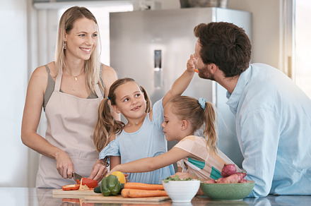 Family, parent and children cooking in kitchen with vegetables for healthy diet, nutrition or meal prep. Bonding, smile and mom, dad and girls learning, teaching and helping cut food ingredients, a Photo by Peopleimages.com