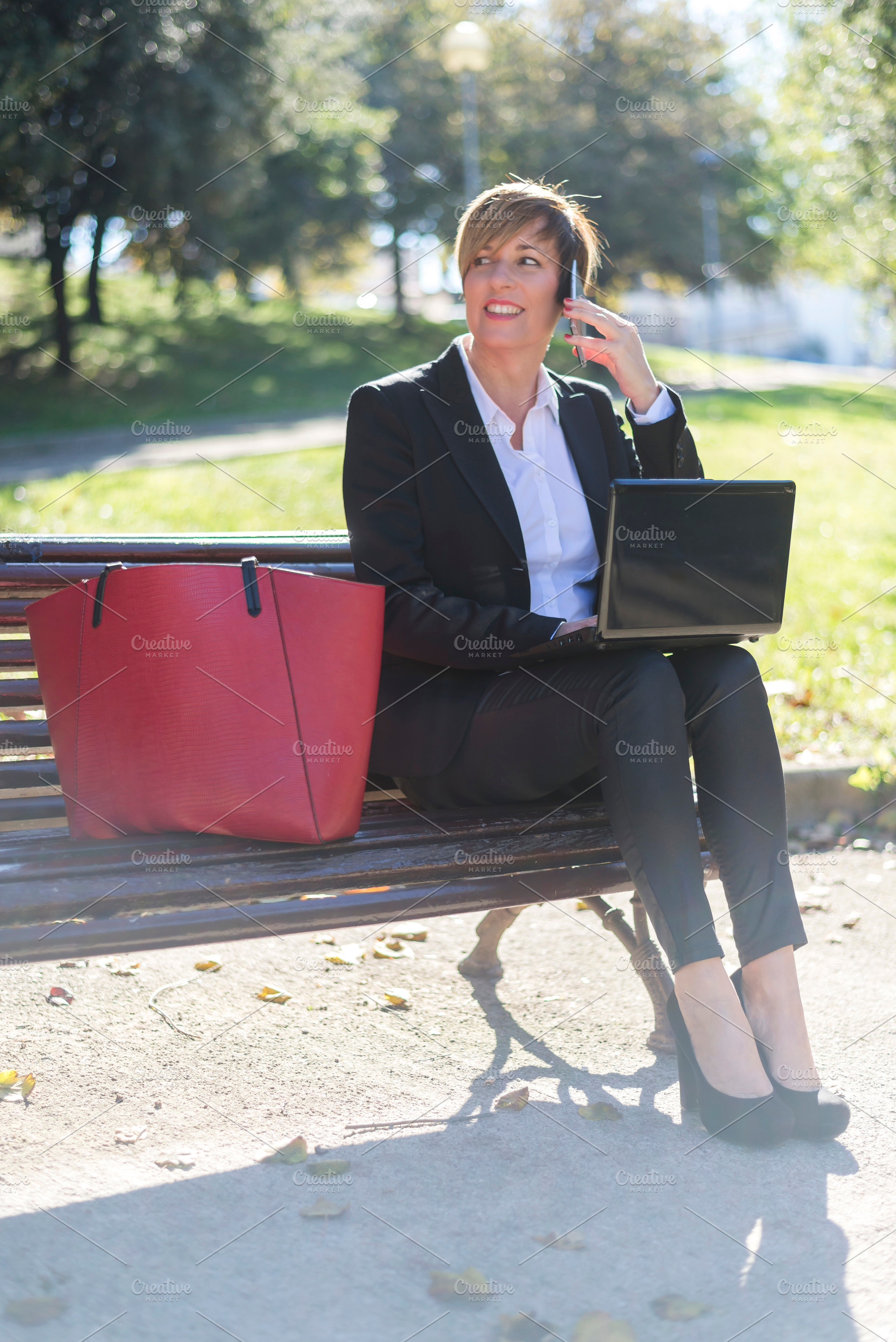 Businesswoman calling with laptop in sunny park, a Photo by RF Images