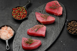 Raw tuna pieces on a black board, spices nearby, a Food & Drink Photo by ndanko