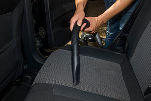 a man vacuums the fabric seat of a car, a Photo by Nito
