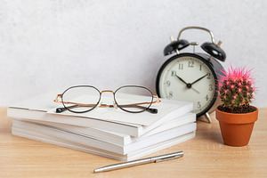 Eyeglasses resting on stack of notebooks with pen, alarm clock,, a Business Photo by Olena Rudo
