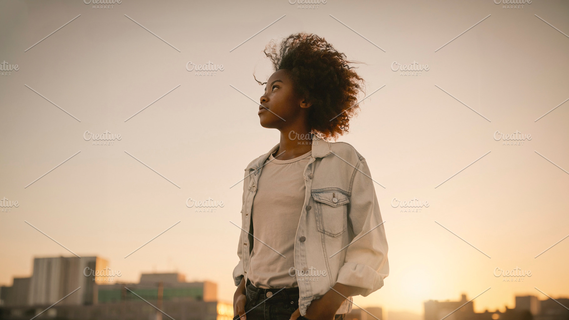 Black woman standing at sunset with city skyline, a Photo by DanFLCreativo