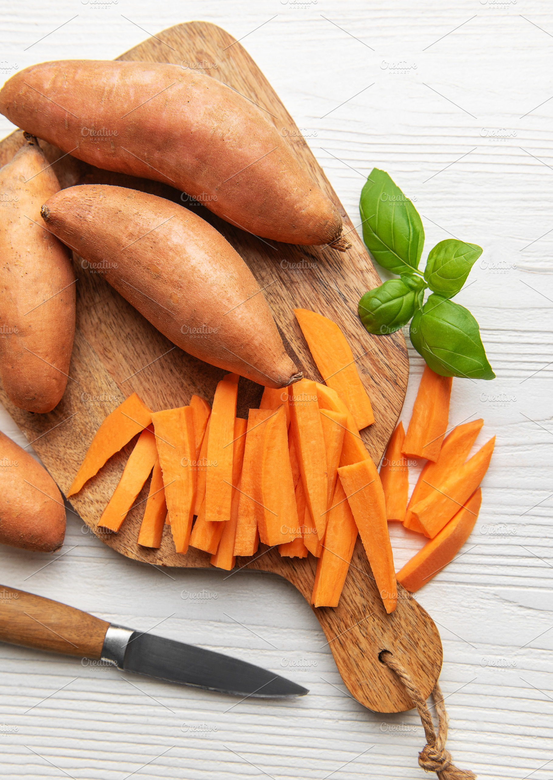 Sweet potato batons on wooden cutting board with basil, a Food & Drink Photo by Olena Rudo
