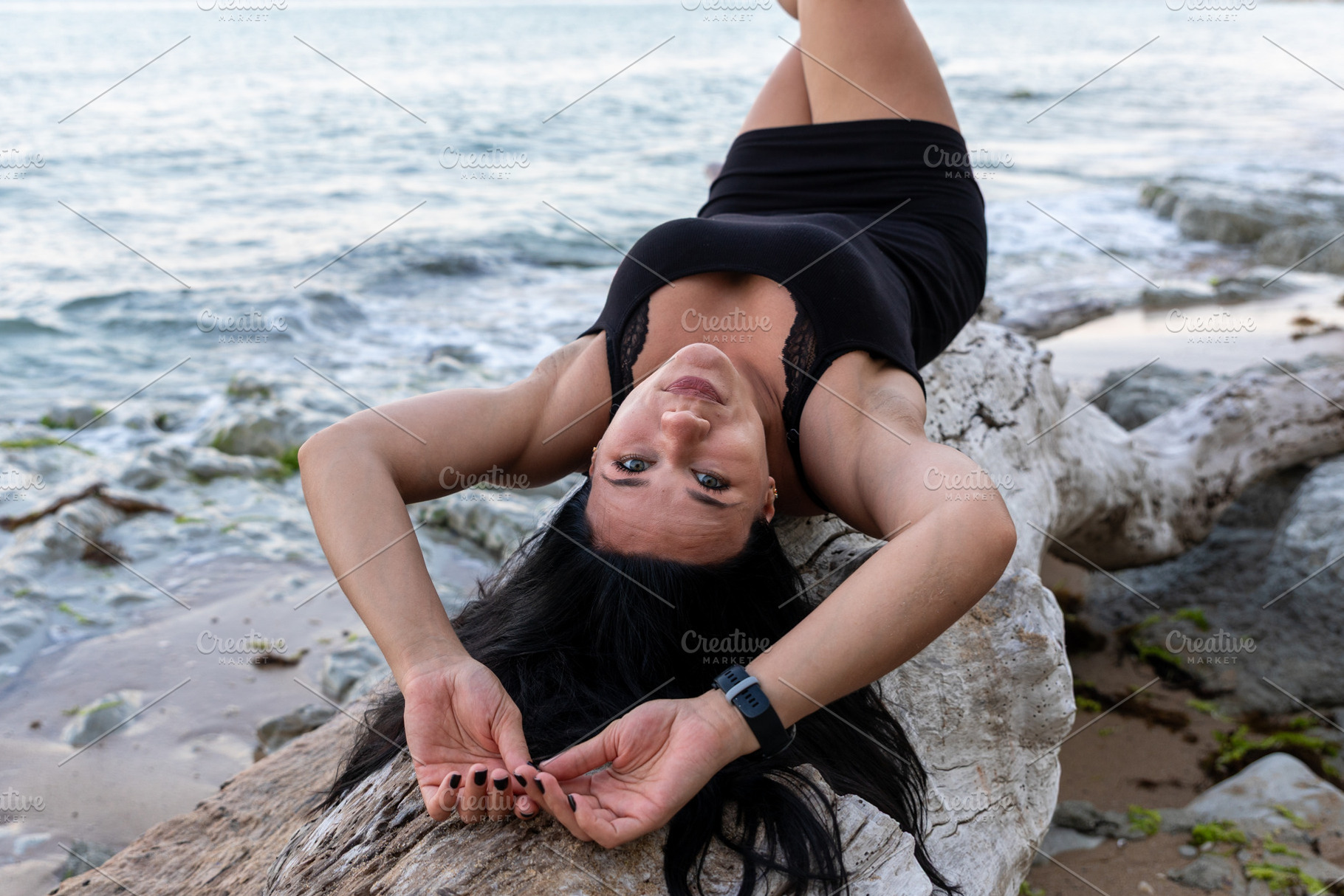 Confident woman in black dress reclining on driftwood by the ocean, enjoying th, a Person Photo by Ales Munt