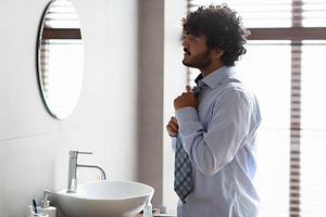 Young indian businessman tying necktie and preparing for work, standing in bath, a Person Photo by Prostock-Studio