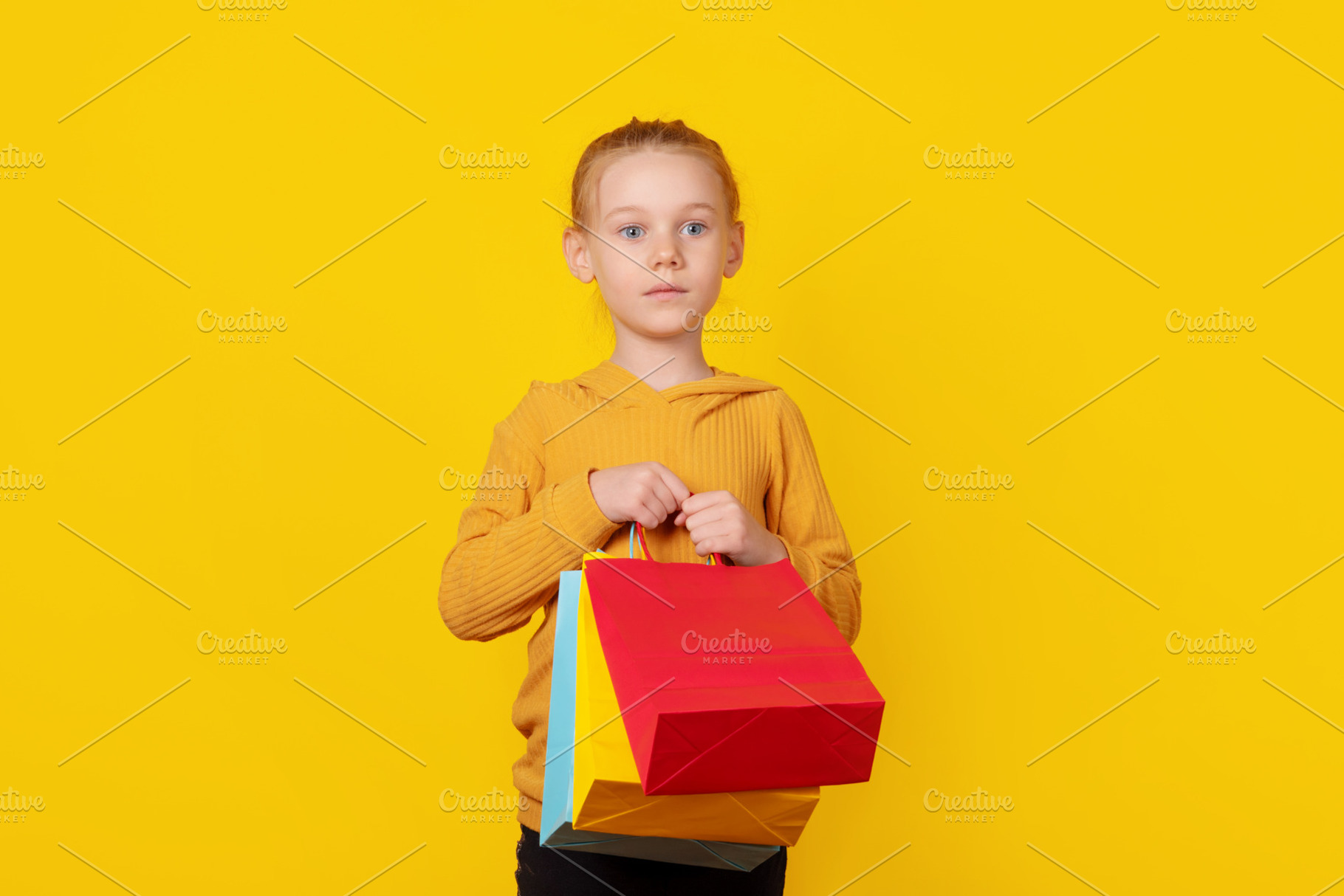Young girl holding colorful shopping bags against bright yellow, a Person Photo by Ales Munt