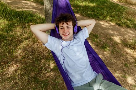 A young guy with curly hair is relaxing on a hammock on a hot summer day., a Person Photo by Photostock