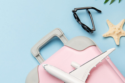 Pink suitcase with toy airplane, sunglasses, straw hat, seashell