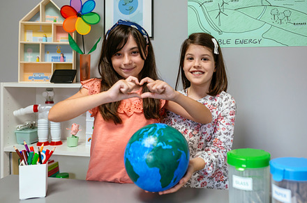 Two female students showing globe world earth while one making heart shape with, a School & Education Photo by davidpereiras