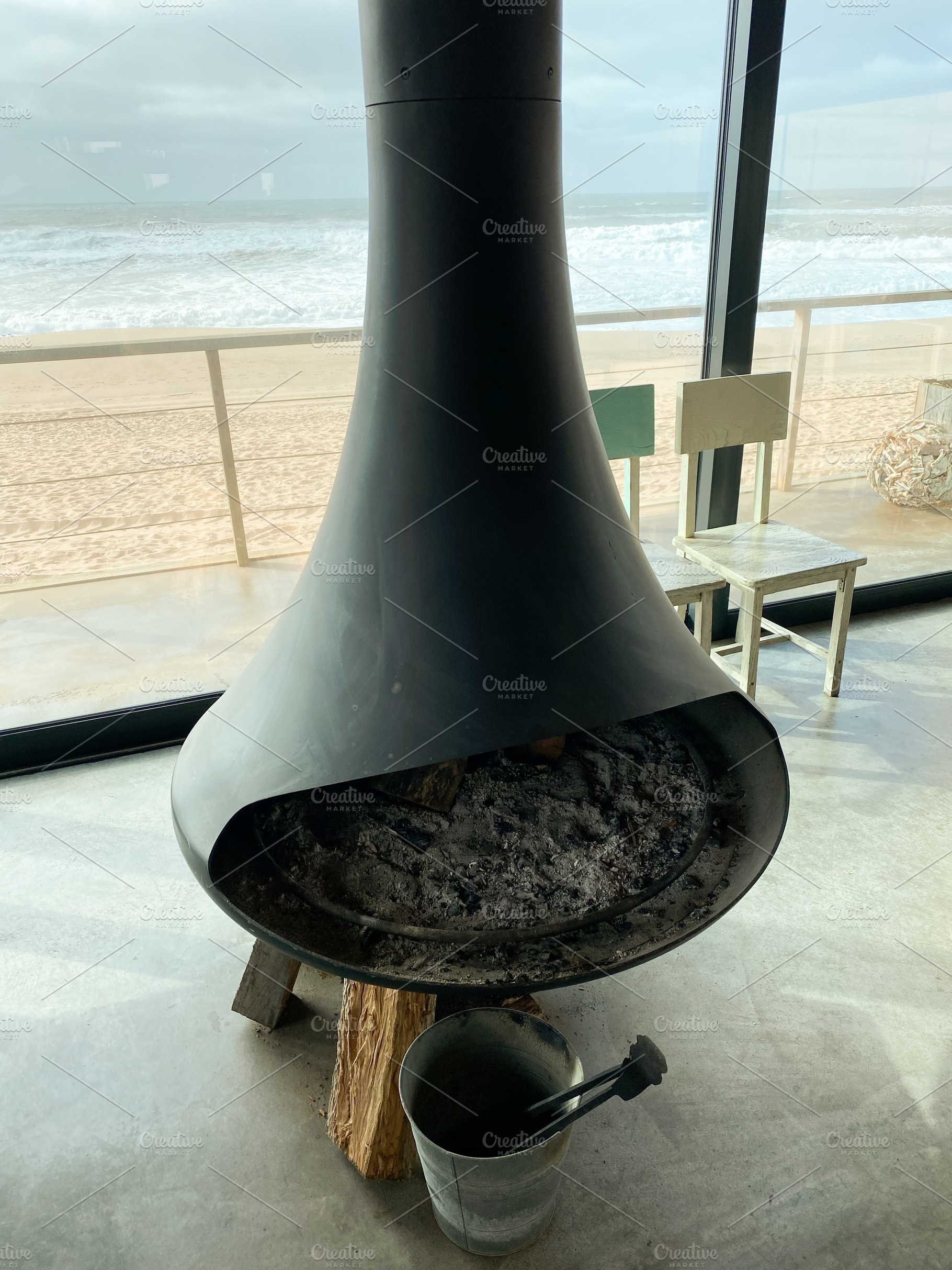 Modern fireplace with ash and logs, framed by ocean waves visibl, a Holiday Photo by sebastianaraw