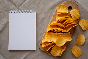 Bacon flavoured potato chips on a wooden board, blank notepad, t, a Food & Drink Photo by LiudmylaChuhunova