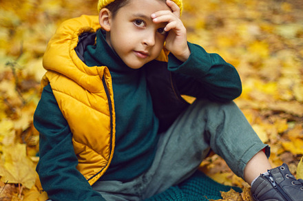 portrait of a fashionable serious child boy autumn sitting on a trail in orange, a Person Photo by SaulichPhoto