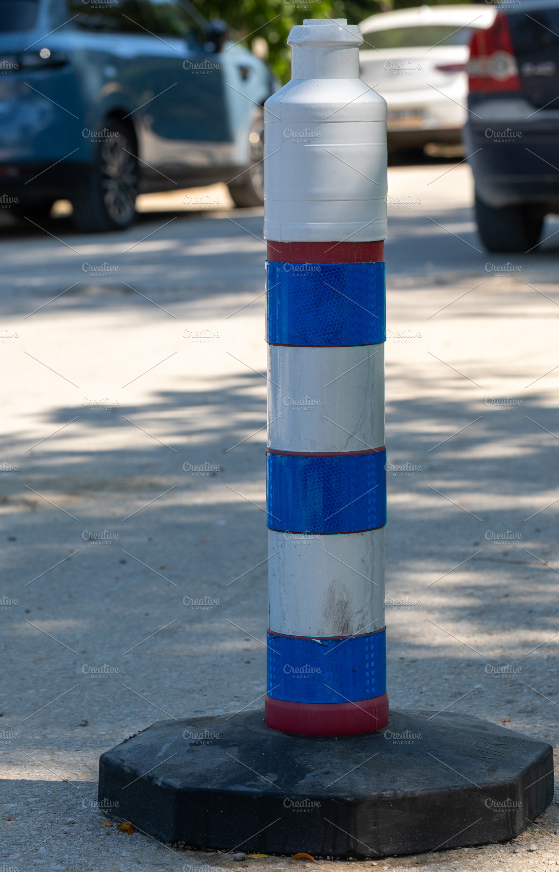 Vertical blue and white striped traffic bollard on pavement, with blurred parke, a Holiday Photo by Ales Munt