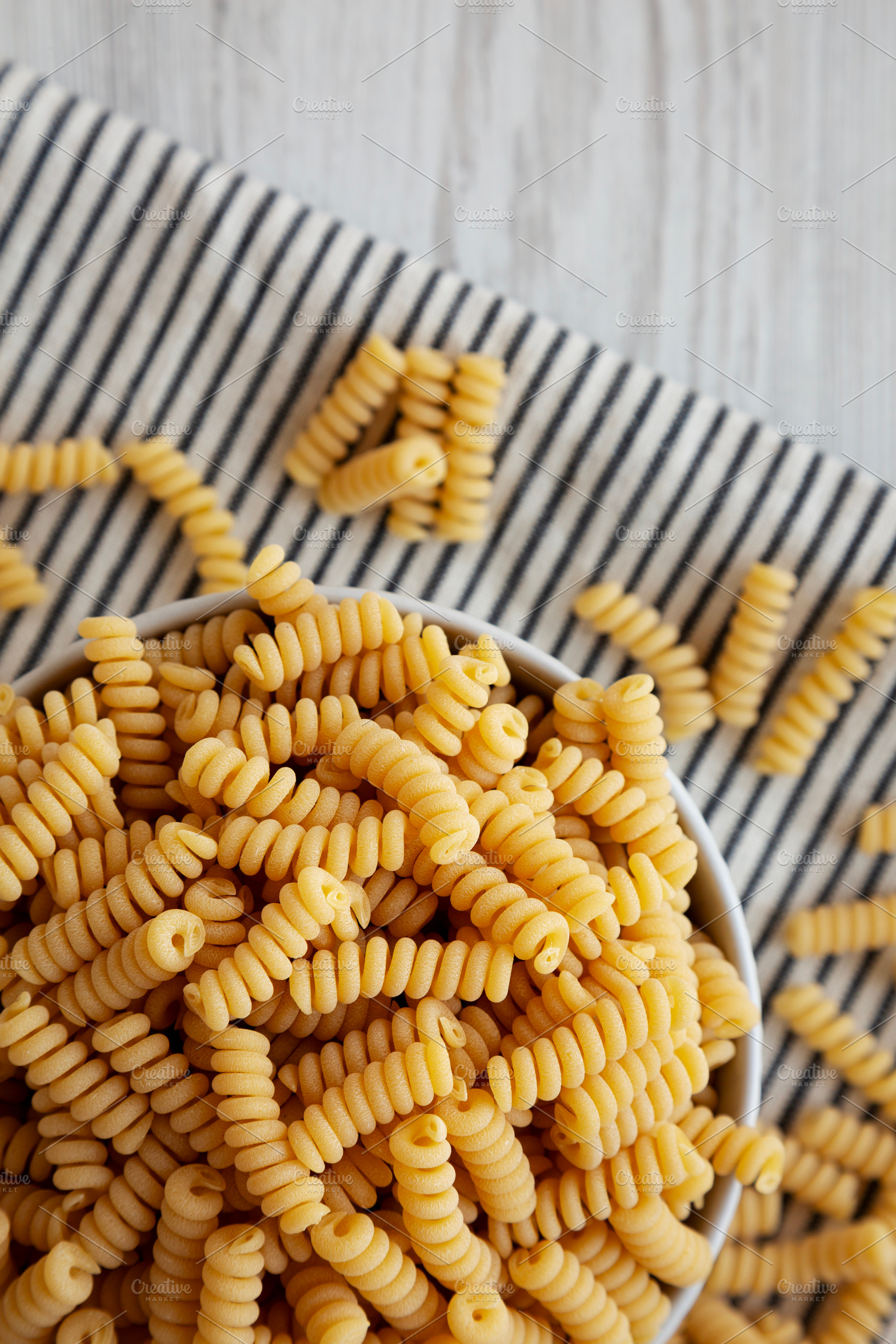 Uncooked Organic Dry Fusilli Pasta in a Bowl, top view. Flat lay, a Food & Drink Photo by LiudmylaChuhunova