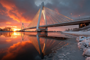 Sunset reflecting on a frozen river with a modern cable-stayed bridge, an Industrial Photo by AS photostudio