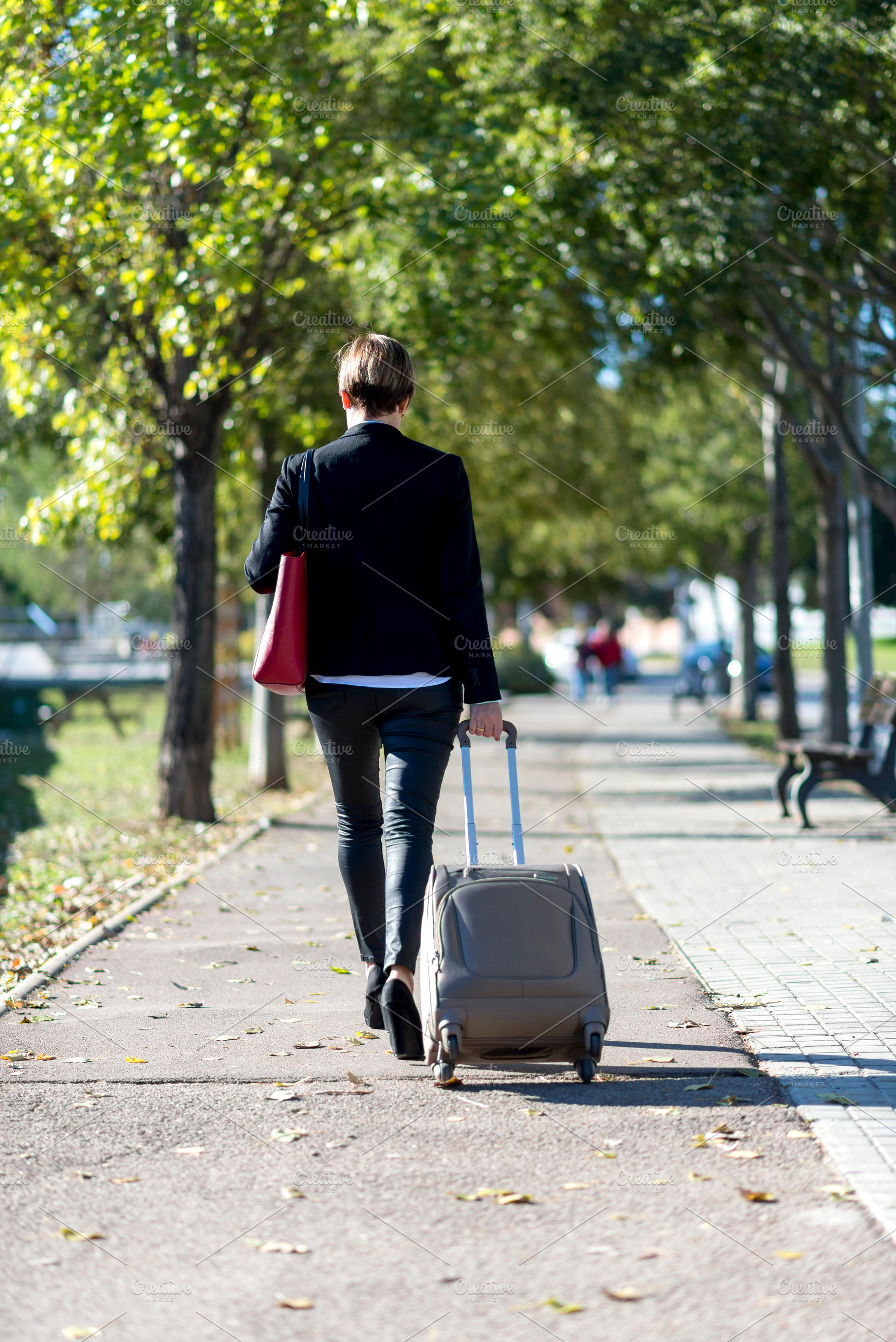Businesswoman walking with suitcase in park path, a Photo by RF Images