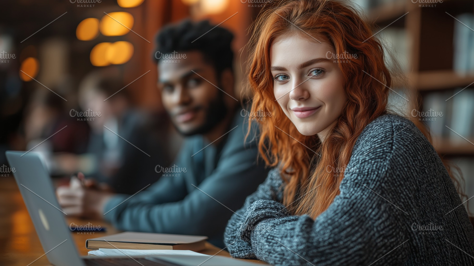 A young Caucasian woman with red hair smiles while studying with friends in a c, a Person Photo by ImageMir