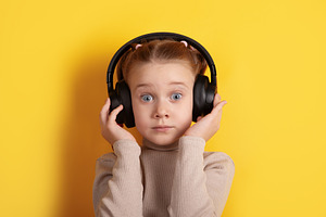 Young girl with headphones on yellow background, expressing surp, a Person Photo by Ales Munt
